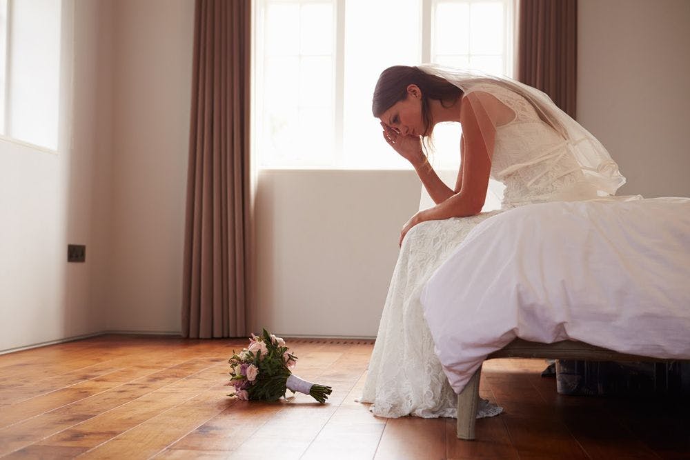 A bride sitting down on a bed looking stressed