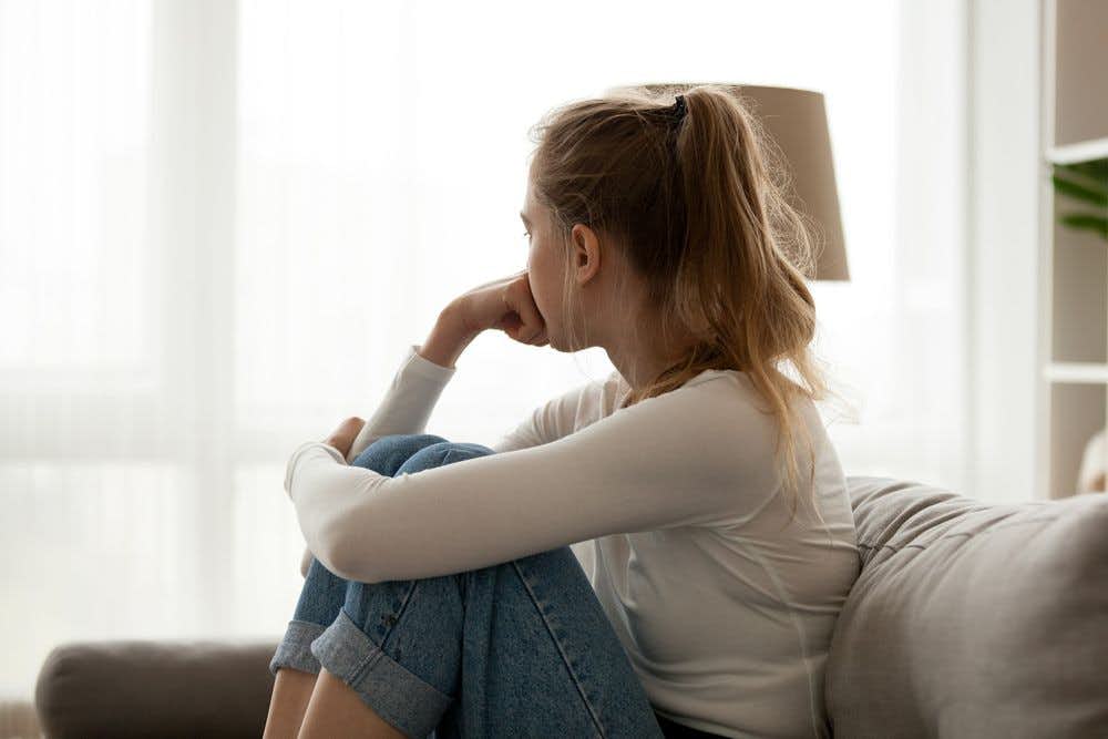 A lonely woman looking out a window while sitting on the couch