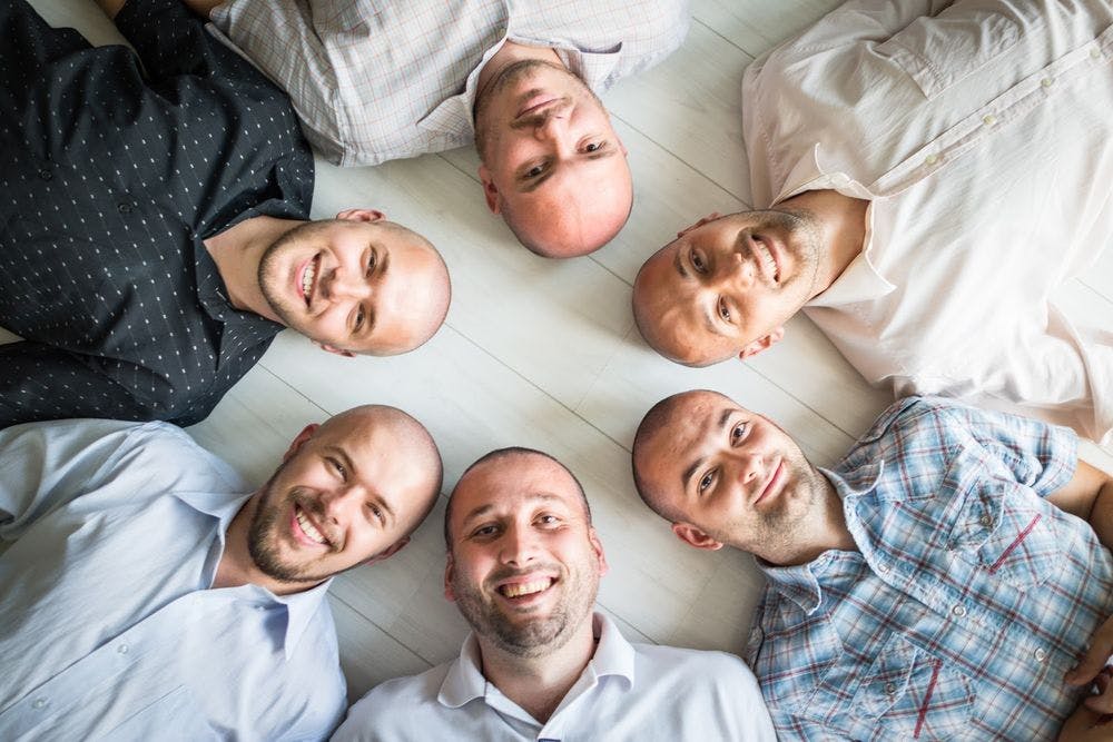 A group of men laying with their heads together in a circle on the floor 