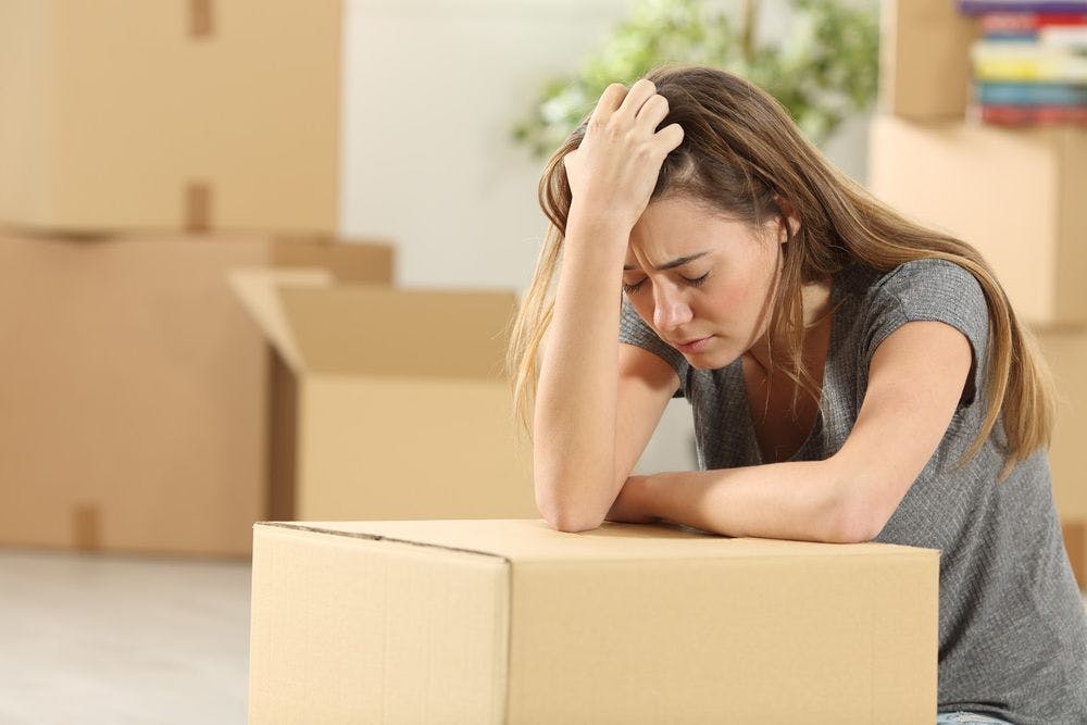 A woman with her eyes closed looking very stressed leaning on a moving box
