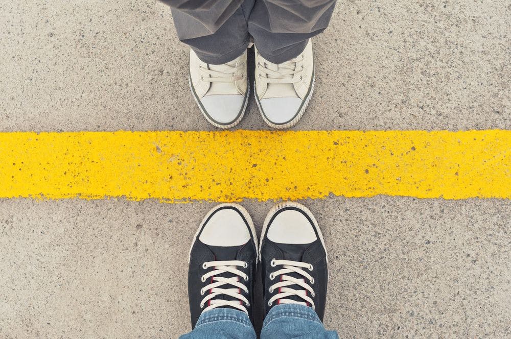 A view of looking down at shoes with another person coming up to a boundary