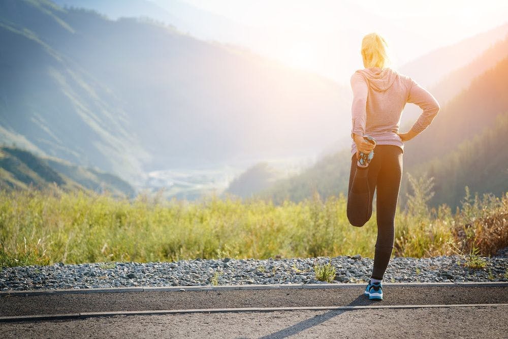 A woman on an open road with mountain scenery, preparing to exercise