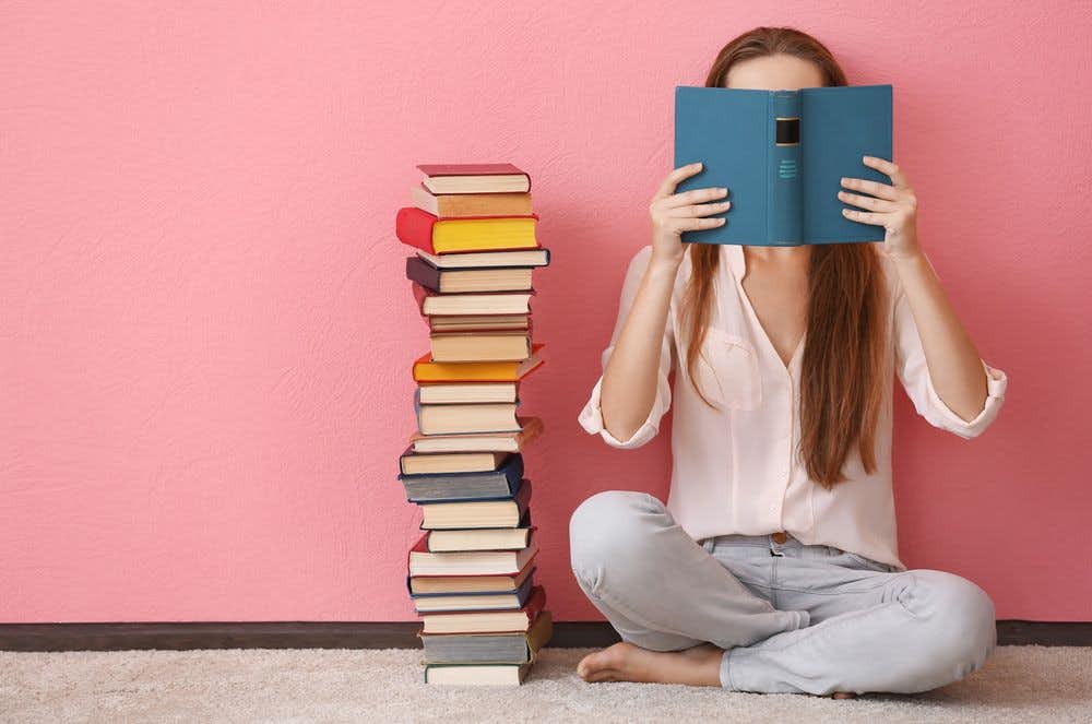 Young woman sitting next to a pile of books, reading