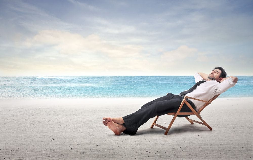 Man in business clothes in a lounge chair vacationing on the beach