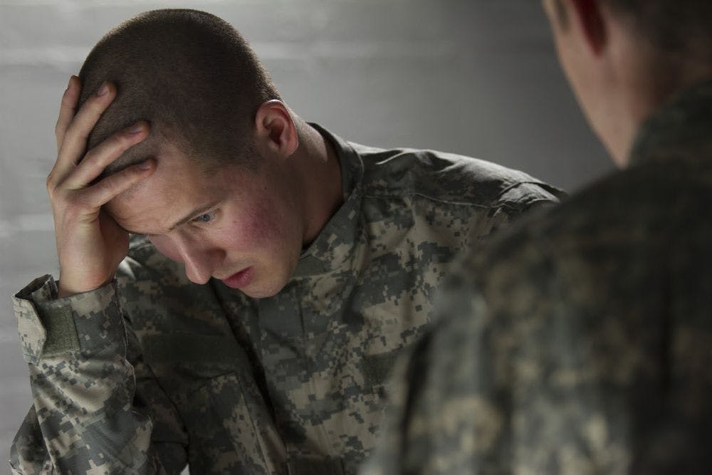 A soldier with his head in his hands, speaking to another about PTSD