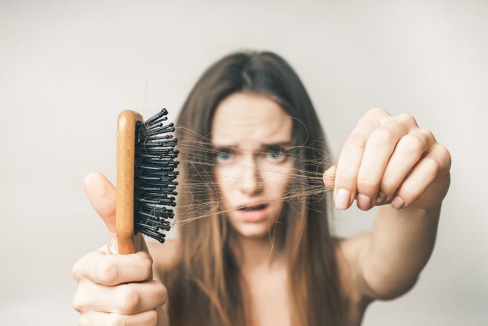 A woman looking at the hair in her hairbrush with concern