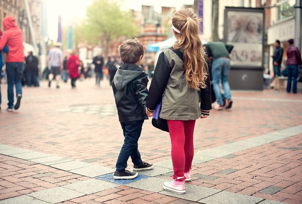 A young boy and girl walking alone in a crowded public square