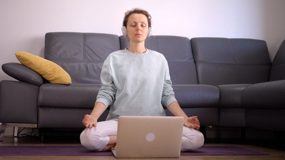 mindfulness guided meditation practicing by woman sitting on floor with headphones and laptop