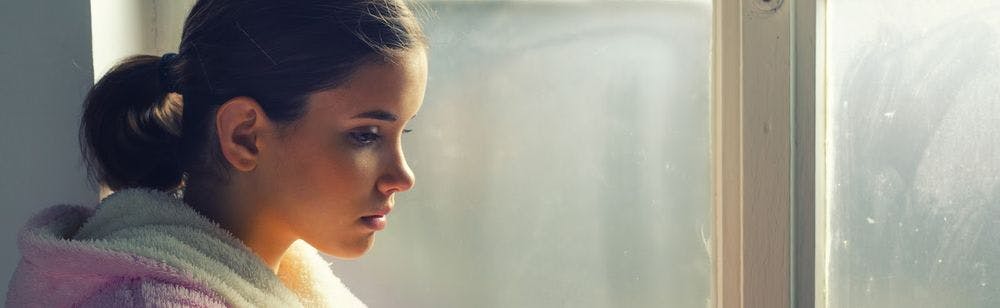 A young girl looking sad by a window