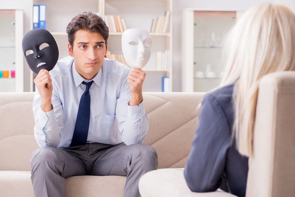 A man in therapy holding two masks, trying to deal with a crisis