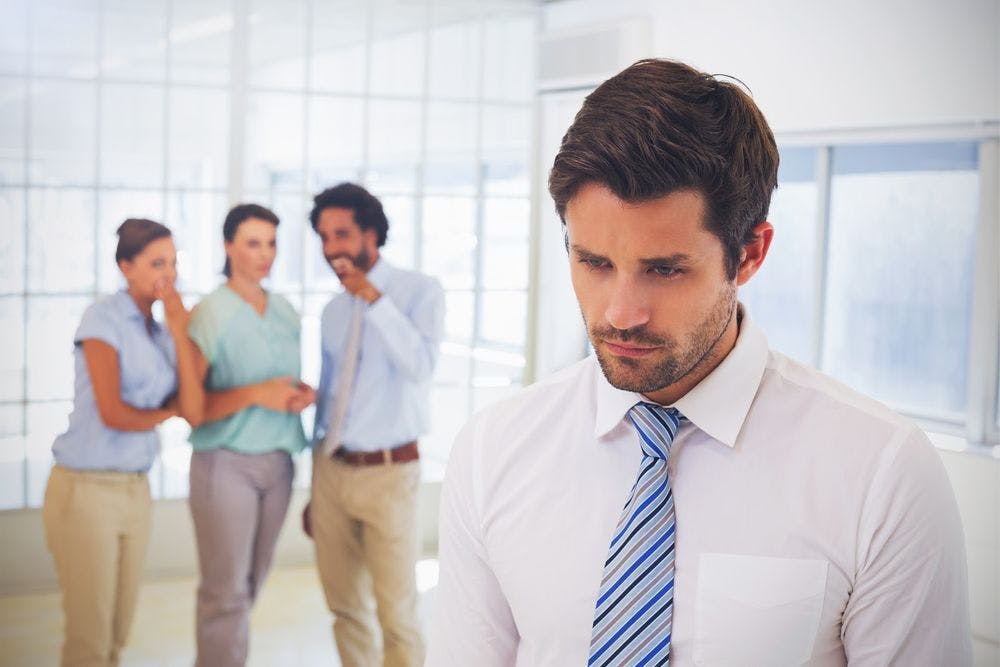 A man looking upset while coworkers whisper behind him