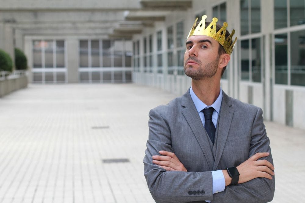A man looking staring at the camera overly confident wearing a crown