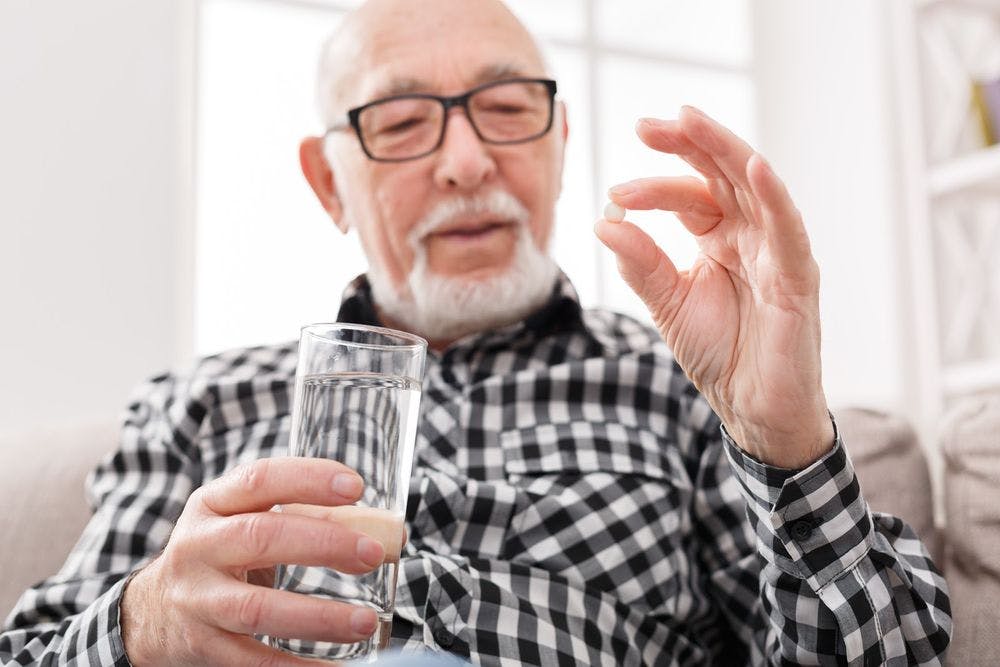 An old man looking at his pill waiting to take it with water