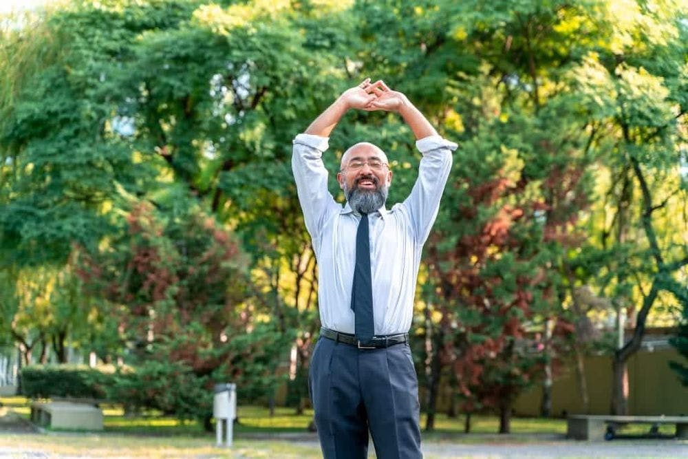 Asian businessman stretching in a park in an urban environment.