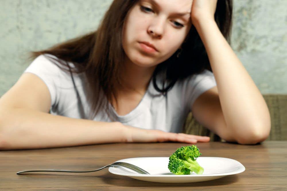 A woman sadly staring at her plate with a single piece of broccoli 