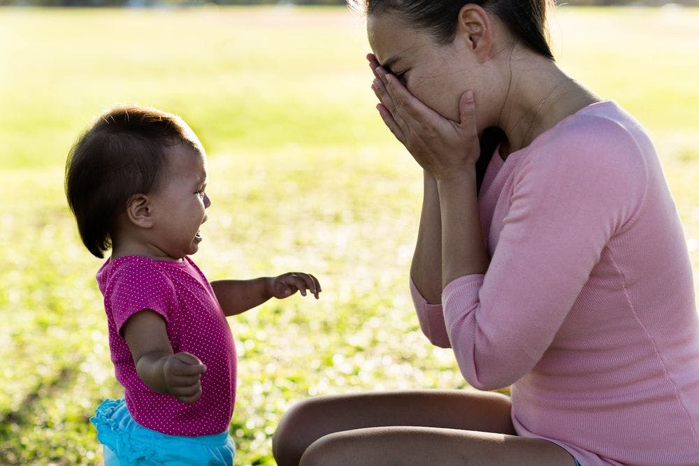 A crying baby looking at her mother in a field, covering her face crying