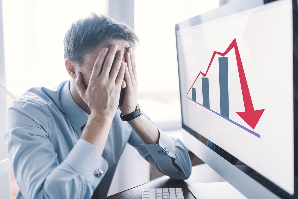 A man looking stressed at a downward trending graph on the computer