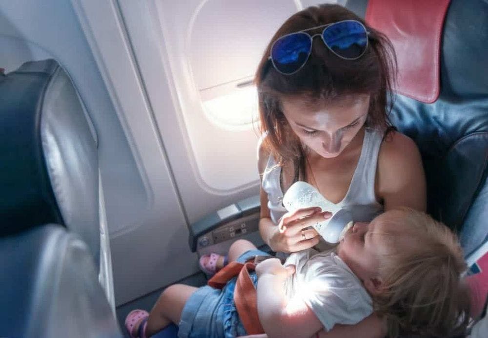 Young mother feeding her small daughter from bottle on airplane