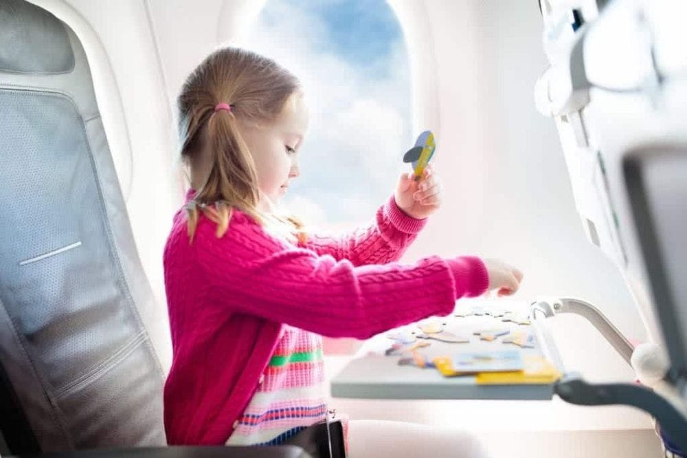 Child in airplane. Kid in air plane sitting in window seat. Flight entertainment for kids. Traveling with young children. Kids fly and travel. Family summer vacation. Girl with toy in airplane.