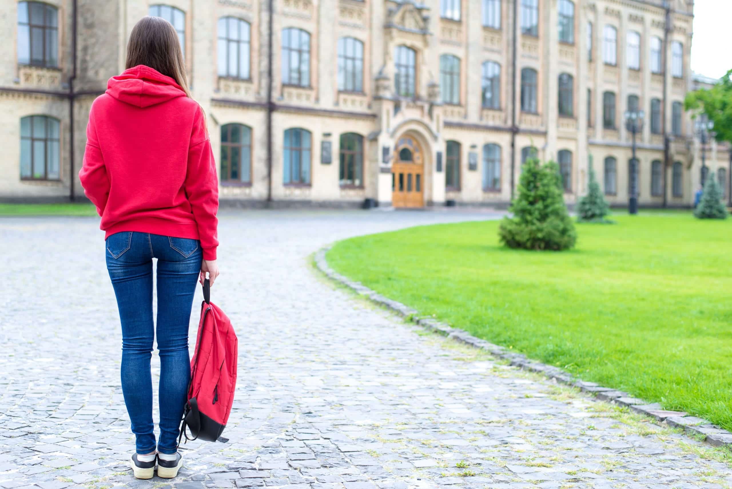 Back rear behind full length bosy size photo of serious confident concentrated hipster holding schoolbag in hand looking at the entrance standing near green lawn