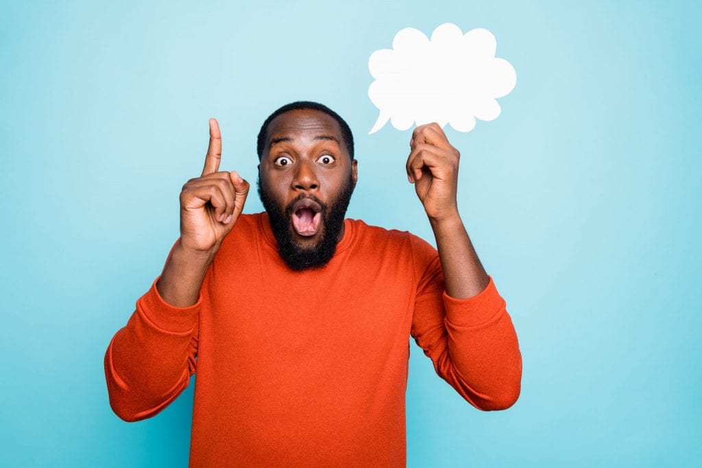 Photo of funny cheerful mixed-race man showing his forefinger up with amazement on face holding white bubble of thoughts isolated, vivid blue color background