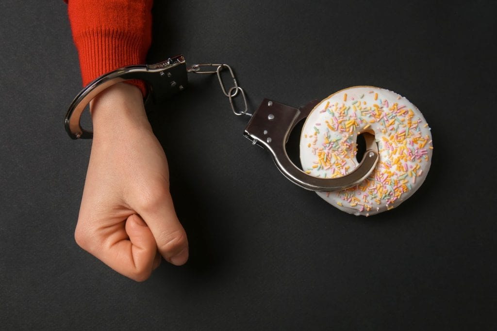 Woman handcuffed to tasty doughnut on dark background. Concept of addiction