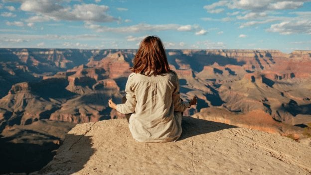woman sitting on the peak of a mounting meditating taking deep breaths