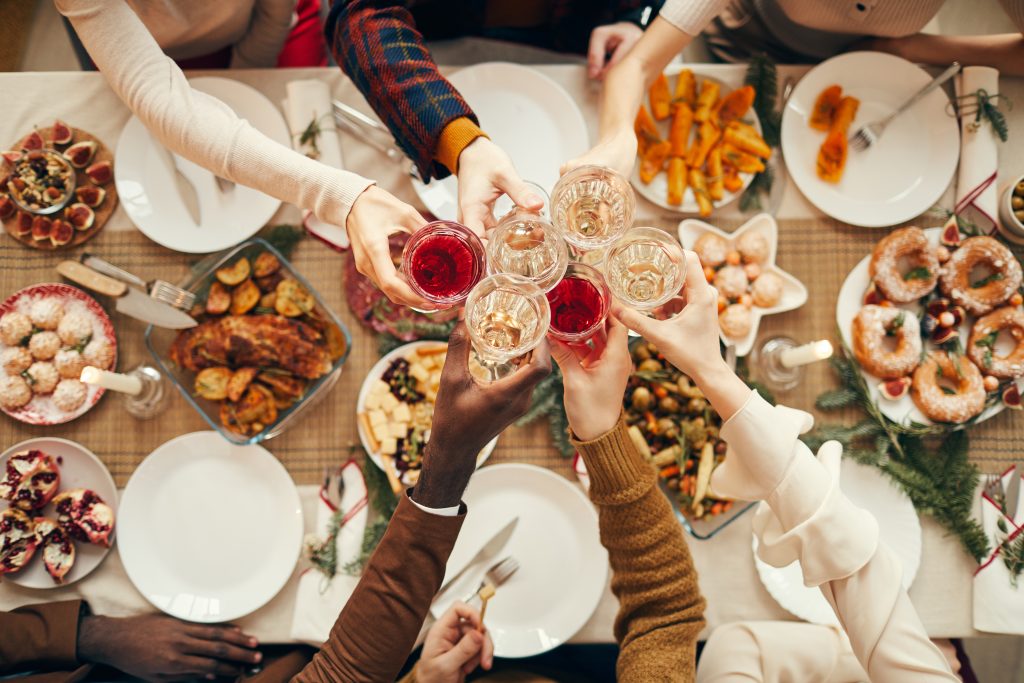 People raising glasses over festive dinner table while celebrating Christmas with friends and family, copy space